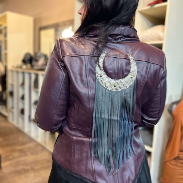 The back of a burgundy leather motorcycle jacket. A textured lunar moon emblem with long black fringe attached to the bottom takes up the back of the jacket.
